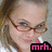 Pixelated close-up of a person with light skin, brown hair tied back, wearing thin-framed glasses and pink lipstick, smiling slightly.