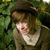 A pixelated image shows a person with brown hair wearing a dark hat and light-colored shirt against a green background.
