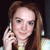 A pixelated close-up of a person with long brown hair holding a white phone to their ear against a dark background.