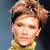 Pixelated close-up of a person with light brown hair styled upward, wearing a yellow garment against a blue and dark background.
