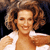 Pixelated image of a person with curly brown hair wearing a white collared shirt, smiling with eyes closed against a dark background.
