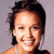 Pixelated portrait of a person with dark hair and light skin smiling against a gray background.