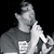 Pixelated grayscale image of a person in profile with hand near mouth, wearing dark shirt and light sleeves against black background.