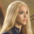 Pixelated close-up of a person with long blonde hair wearing a dark blue top against a brown background.