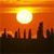 Pixelated sunset scene with bright yellow sun above dark city skyline silhouette against orange gradient sky.