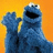 Blue Muppet-like character with raised hand against orange background, blue text 'michele' top-right and 'likes ccookies' bottom on solid blue field.