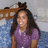 A pixelated image shows a person with long dark hair wearing a purple top, standing against a blurred background with blue and brown tones.