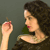 A pixelated image shows a person with curly dark hair holding a small red object near their face against a muted green background.