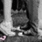 A grayscale pixelated image shows a partial view of a figure with dark hair and light clothing, standing near vertical structures.