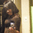 A pixelated image shows a person with long dark hair holding a small object near their chest against a light-colored wall with a visible light switch.