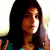 A static pixelated image of a person with long dark hair wearing a blue and teal patterned top against a light background.