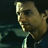 Pixelated close-up of a person's face in profile view, wearing a dark jacket with a light-colored collar, against a dark background with greenish horizontal lines.