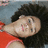 Pixelated image of a person with dark curly hair wearing a red top, lying down with eyes closed and mouth slightly open against a blue background.