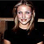 Pixelated image of a person with light brown hair wearing a dark shirt against a black background.