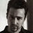 Pixelated grayscale portrait of a person with short dark hair, wearing a dark collared shirt against light and dark background sections.