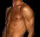 Static pixelated image of a shirtless muscular male torso with visible chest hair and shoulder highlights against dark background.