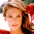 A pixelated close-up of a person with light brown hair wearing a red garment, set against a blurred background with green and white tones.