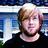 Pixelated image of a person with light brown hair and fair skin wearing a dark top against a blue and white background.