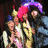 Group of people wearing colorful hats with pink, purple, and blue feathers; one person holds a golden helmet-like prop.