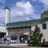 Pixelated static image of a building with a tall tower, dark windows, and green roof trim under a blue sky with clouds.