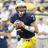Pixelated image of a football player in dark blue jersey and yellow pants holding a football, with yellow background text reading '2008 National Champions'