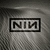 Static pixel art icon with a gray gradient background and a black rectangular border containing the letters NIM in bold black font.
