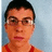 A pixelated image of a person with short dark hair and glasses, wearing an orange shirt with red straps, next to green background text reading 'this guy is ugly'.