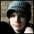 A person wearing a dark beanie and black top against a brick wall background, with subtle facial expression changes between frames.