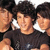 Group of people in dark shirts with white collars, some faces partially visible against a light background.