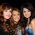 Three women pose together in a group photo with varied clothing and background elements
