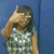 Pixelated image of a person with dark hair wearing a light-colored patterned top, raising their right hand near their face against a blue background.