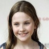 A young girl with light brown hair smiles at the camera, wearing a dark blue sleeveless top against a plain white background.
