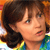Pixelated close-up of a person with brown hair, light skin, and a colorful striped shirt, set against a blurred background with warm tones.