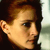Pixelated close-up of a person's face in profile view, showing light brown hair, ear, and side of the head against a blurred background.