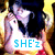 A pixelated image of a person with dark hair holding a white unicorn, with text below changing from 'SHE'z' to 'TENAxO' in blue letters.