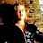 Pixelated static image of a person with light-colored hair and warm-toned skin tones against a black background, rendered in low-resolution 256x256 pixels with visible dithering and color blending.