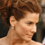 Pixelated close-up of a person with curly brown hair, light skin, and a small earring, cropped to show only the head and upper shoulders against a dark background.