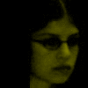 A single person's face appears in three color-filtered variations: yellow, red, and blue, each with dark hair and glasses against a black background.