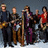 Pixelated group image of five people with instruments and a microphone, surrounded by text listing song titles and band name.