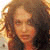 Pixelated close-up of a person with light brown curly hair, wearing a dark top against a light background.