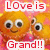Pixelated orange character with large eyes and a smile, pink background, red text reading "Love is Grand!!" at top and bottom.