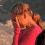 A person in a pink top and dark outer garment covers their face with one hand, then shifts posture while maintaining the hand-over-face gesture across four