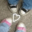 Two pairs of feet in blue jeans and sneakers with pink stripes stand on a textured surface, forming a white heart shape between them.