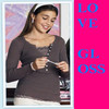 A woman with long brown hair wears a dark gray long-sleeve top and white bottoms, holding a small object while standing against a colorful background with a bright pink vertical panel displaying blue text.