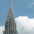 A pixelated image of a tall, pointed building with a spire against a light blue sky and white clouds.