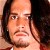 Pixelated close-up of a person with long dark hair, light skin, and a neutral expression against a dark background.