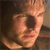 Pixelated close-up of a person with light brown hair, wearing a dark shirt, against a dark background with a lighter area on the right.