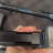 Pixelated image showing a hand holding a dark cylindrical object with a light-colored top against a blurred background.