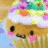 Pixelated cartoon character with brown face, pink cheeks, black eyes, and a white hat under colorful background.