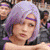 Pixelated image of a person with light purple hair wearing a purple headband and dark clothing, set against a blurred background with indistinct figures.